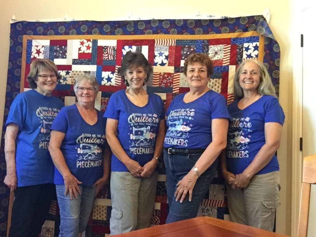 Piecemakers with their new T-shirts in front of the Quilt of Valor top.